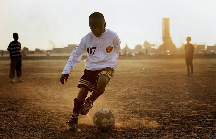 In an African township, Roto Seleke, 11, kicks a ball around in the dirt.. Kate Holt.