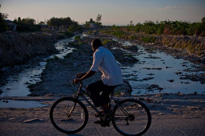 A man cycles passed a river that is heavily polluted and runs passed a camp for displaced people in Port au Prince. Kate Holt.