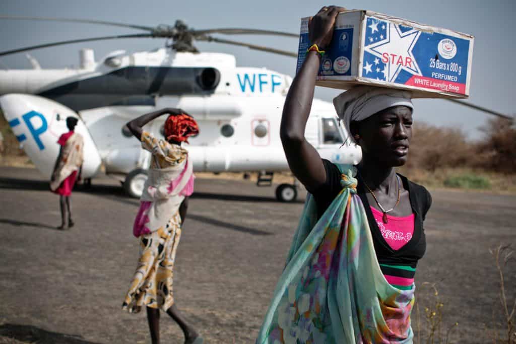 Women carry emergency food supplies on their head from a World Food programme helicopter that has just landed in Thanyang. Kate Holt.
