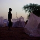 A young boy stands by his mosquito net that is his families only shelter at night, in Thanyang. Kate Holt.